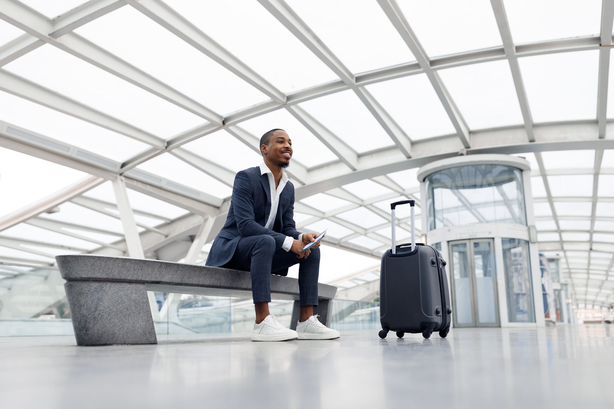 Air Travels Concept. Smiling African American Male Sitting On Bench At Airport