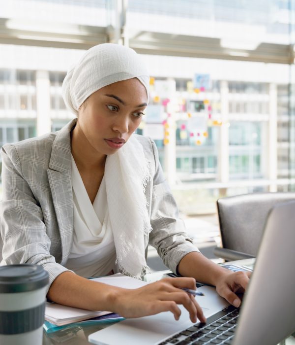 Businesswoman in hijab working on laptop at desk in a modern office